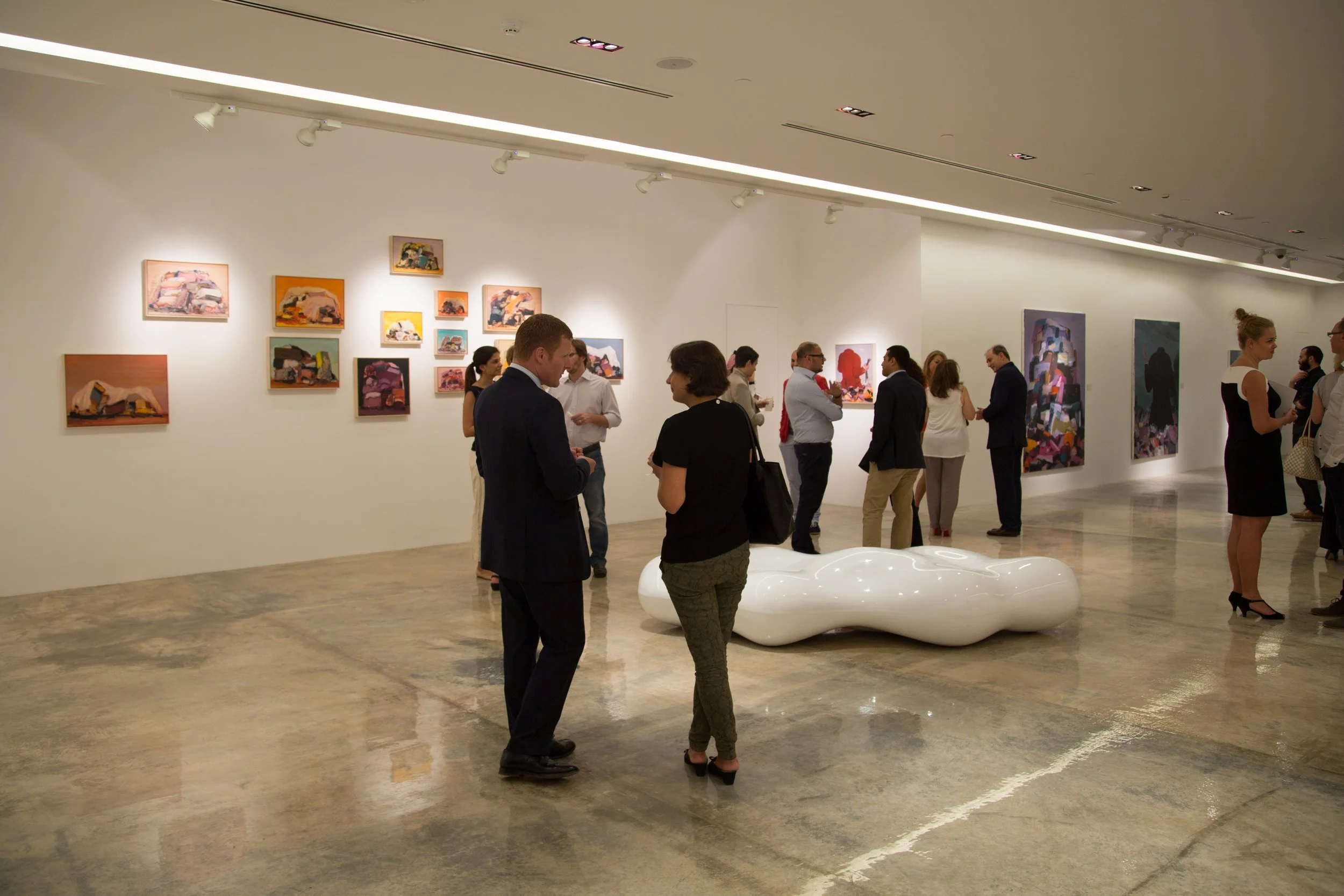 People viewing artwork in an art gallery, with one person talking to another near a white, abstract, curvy sculpture.