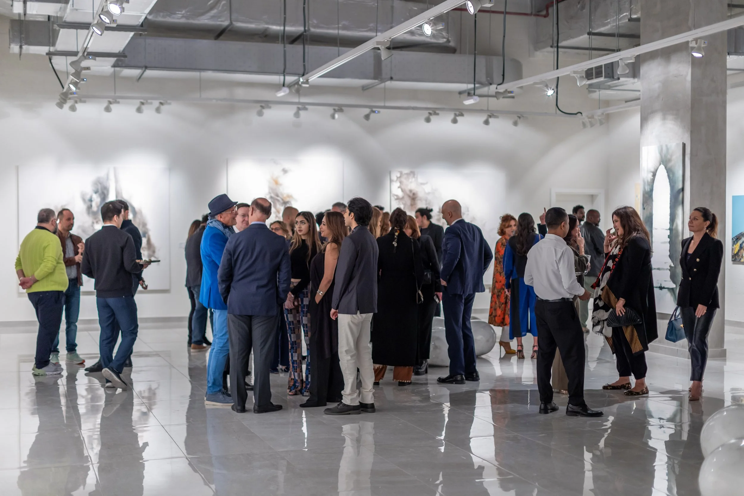 People attending an art gallery or museum exhibition, engaging and viewing artwork on white walls with spotlights overhead.