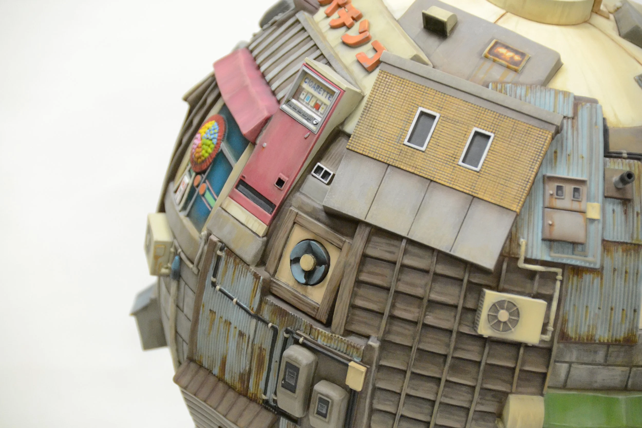 Close-up of a detailed miniature model of a weathered building with a red vending machine, air conditioning units, vents, and windows, against a white background.