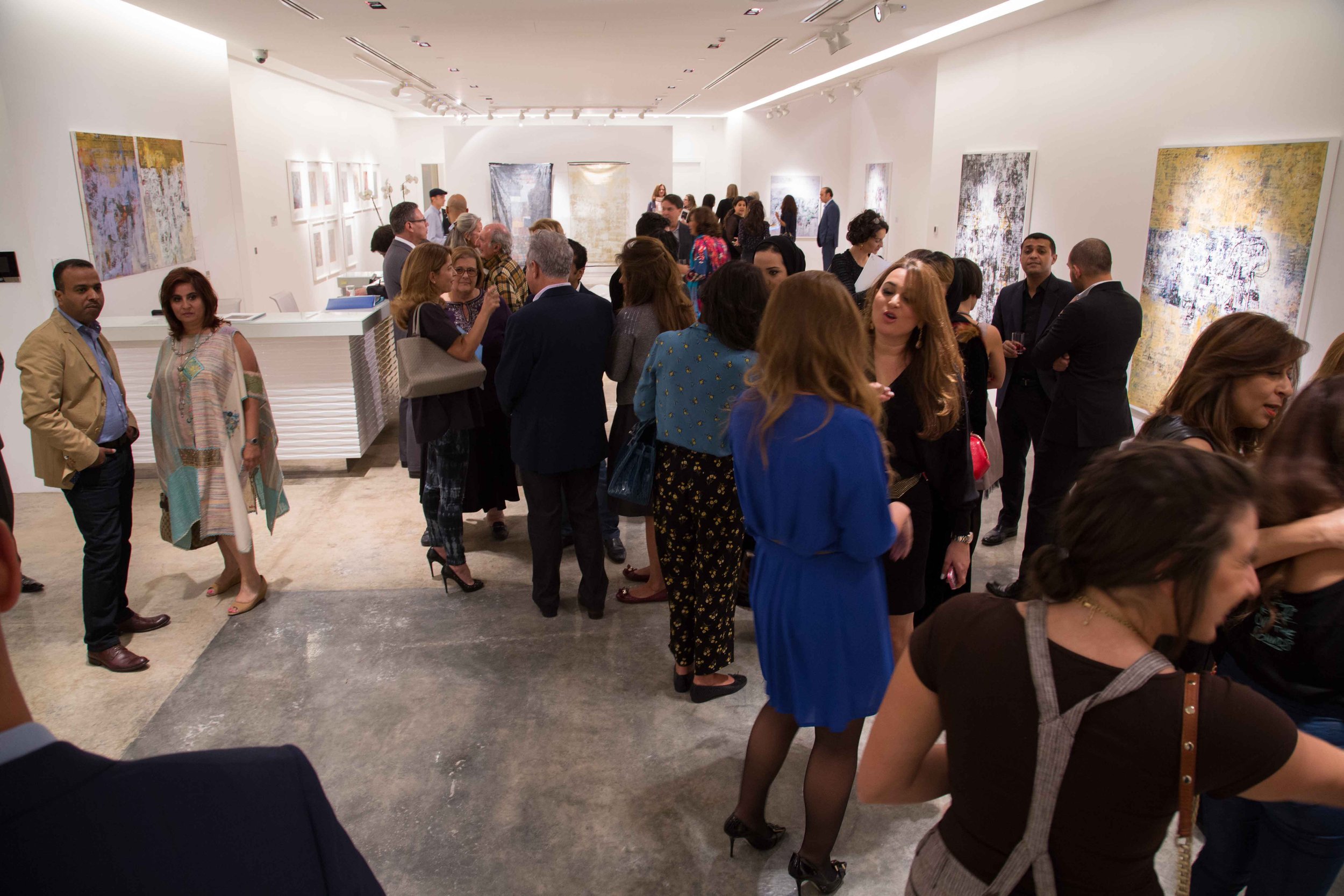 People attending an art exhibition in a gallery, observing and discussing abstract paintings hung on white walls.