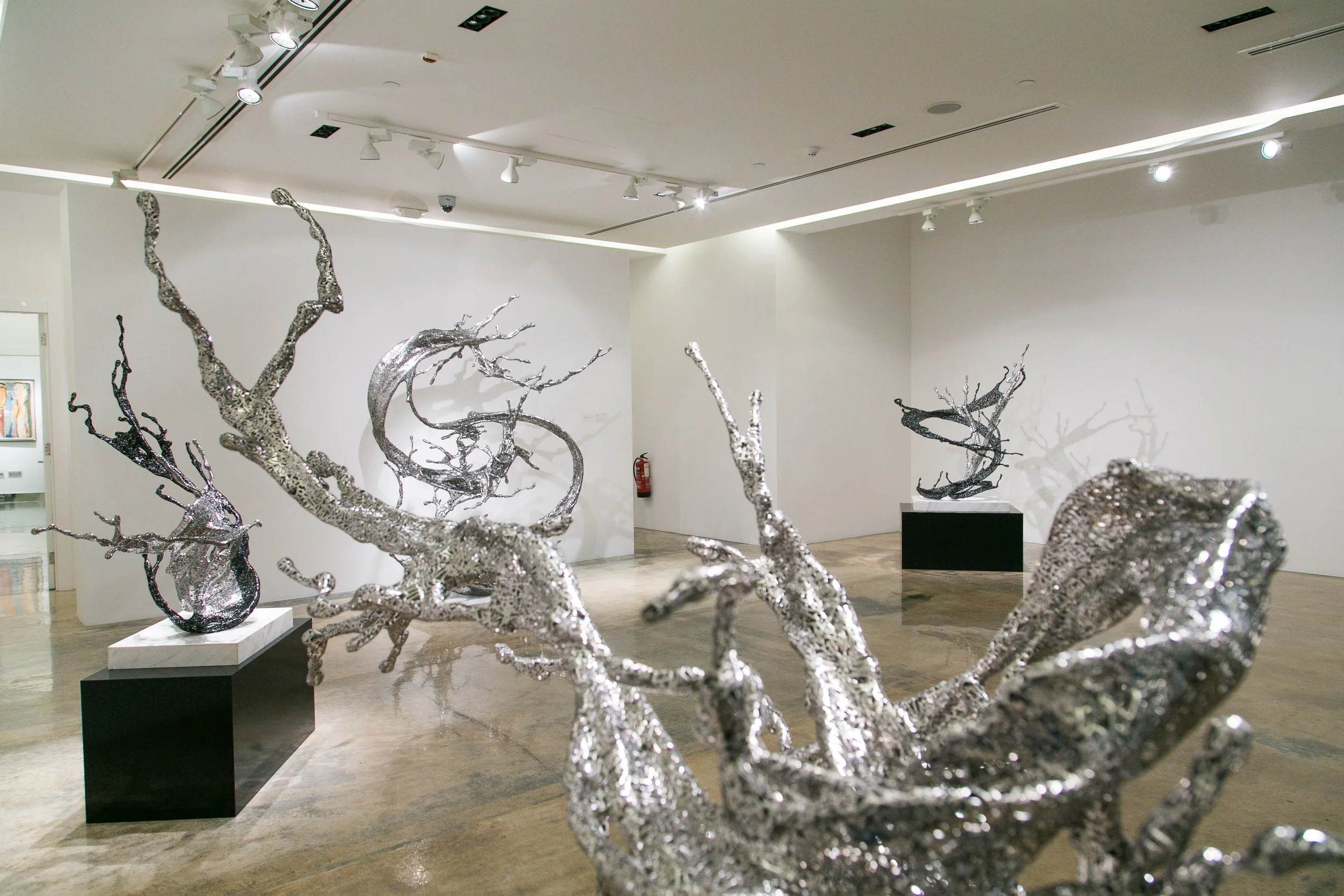 Contemporary art gallery showcasing metallic sculptures that resemble twisted, organic tree branches.