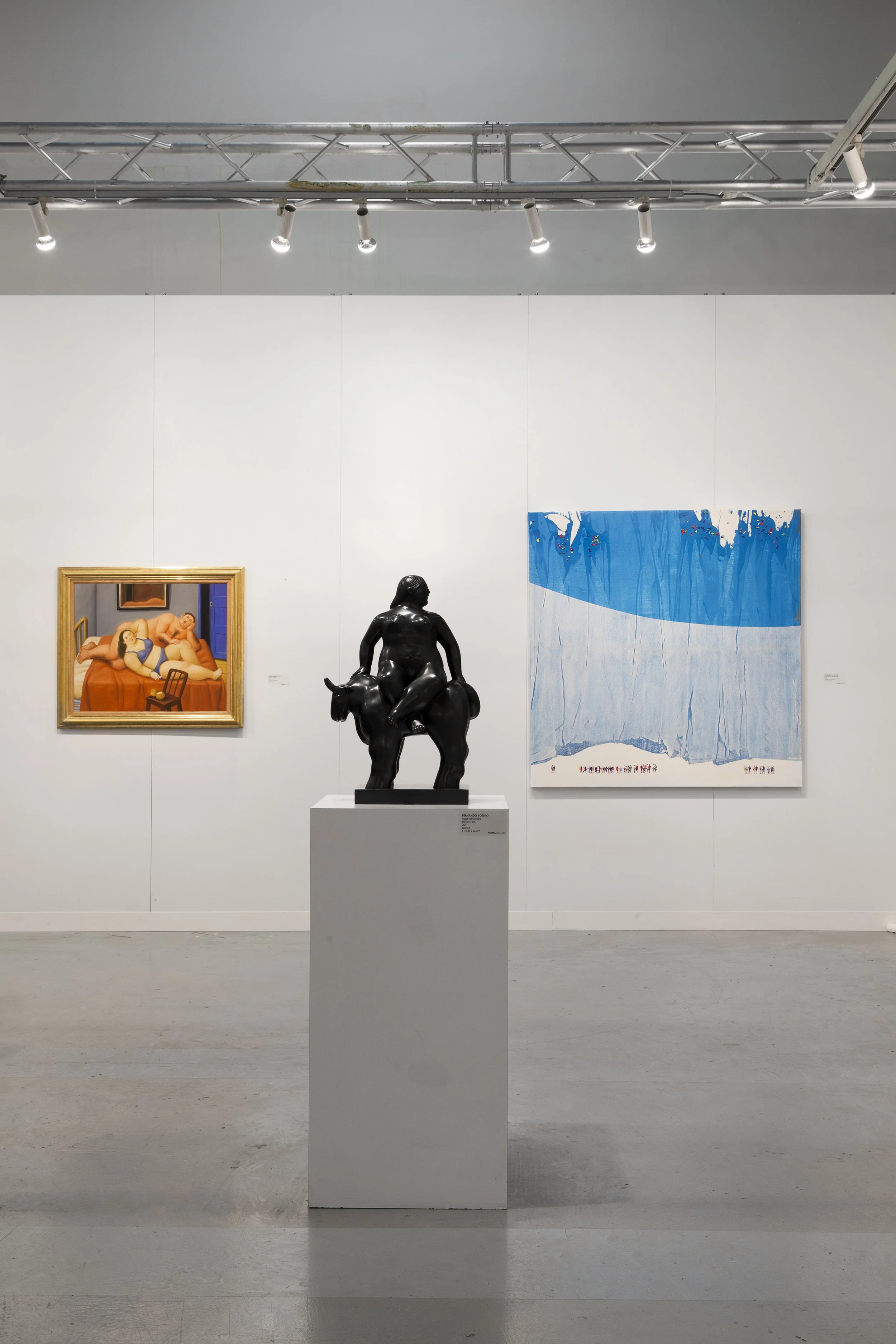 Art gallery with a black sculpture of a person riding an animal on a white pedestal, a colorful painting of reclining figures on the left, and an abstract blue and white painting on the right, illuminated by gallery lights.