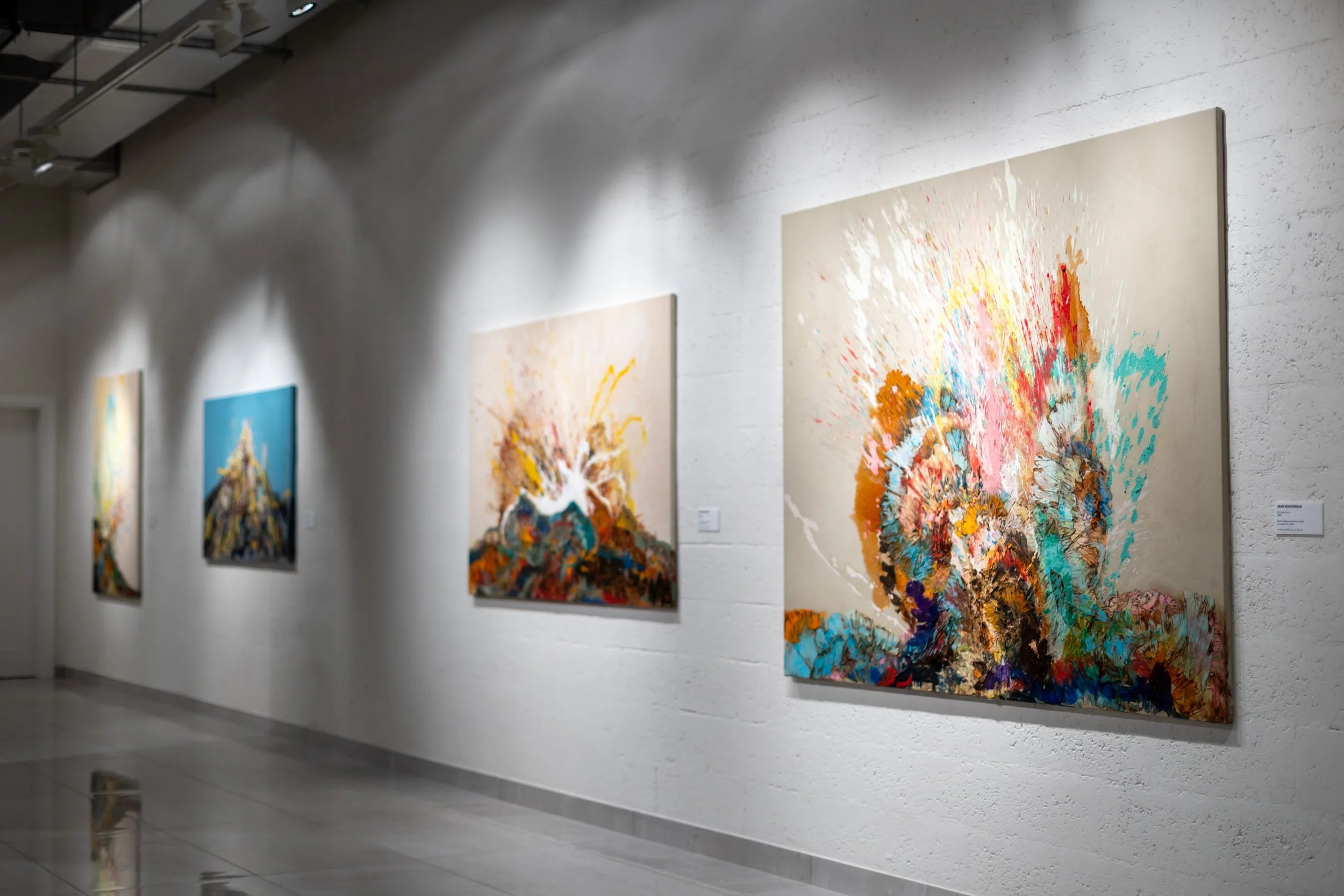 Abstract paintings displayed on a white gallery wall, with spotlights highlighting each piece.