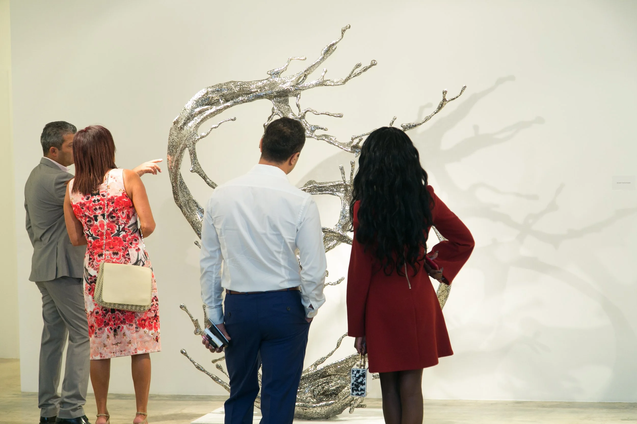 Group of four people observing a metallic abstract sculpture in an art gallery.