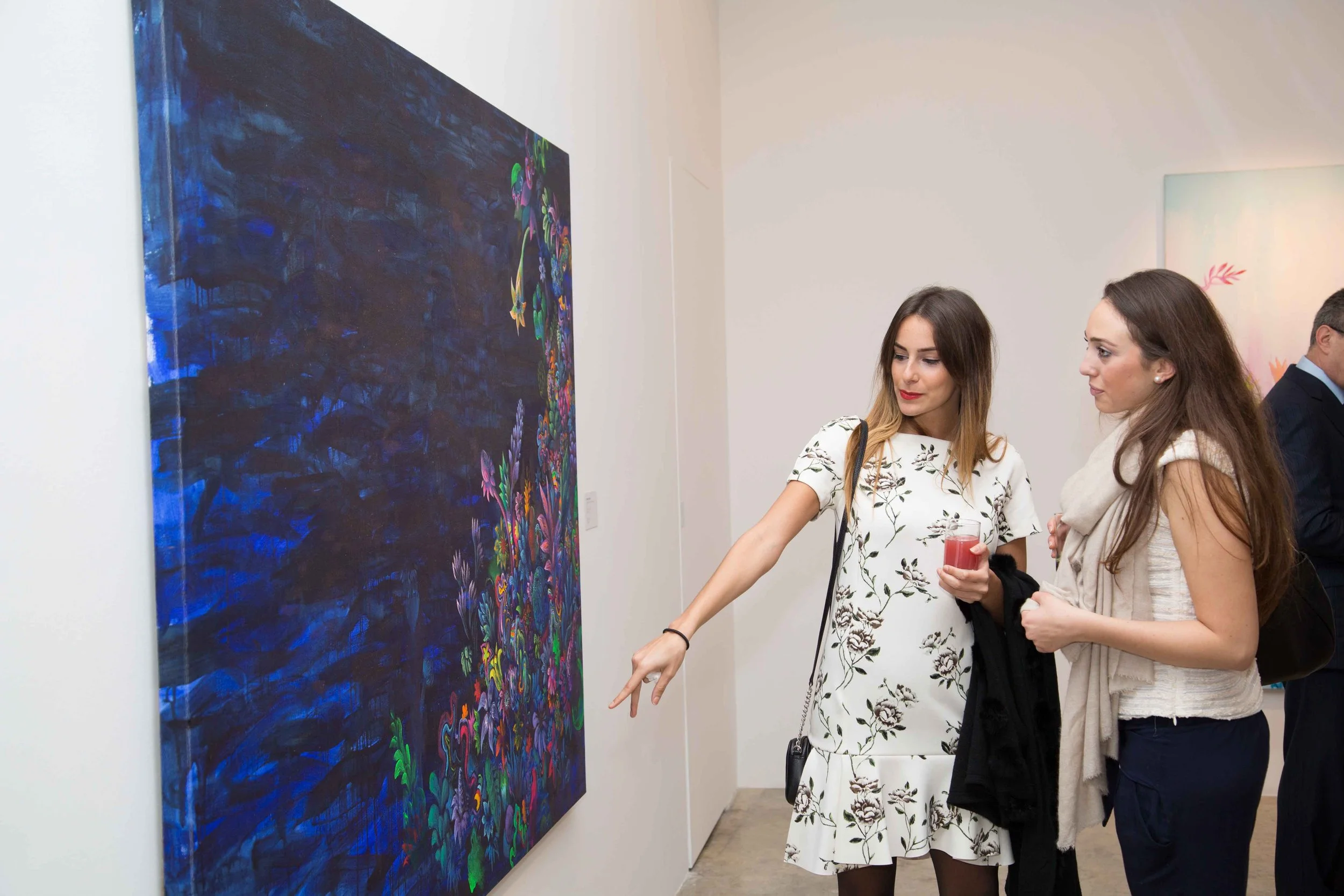 Women viewing a large, colorful abstract painting at an art gallery.