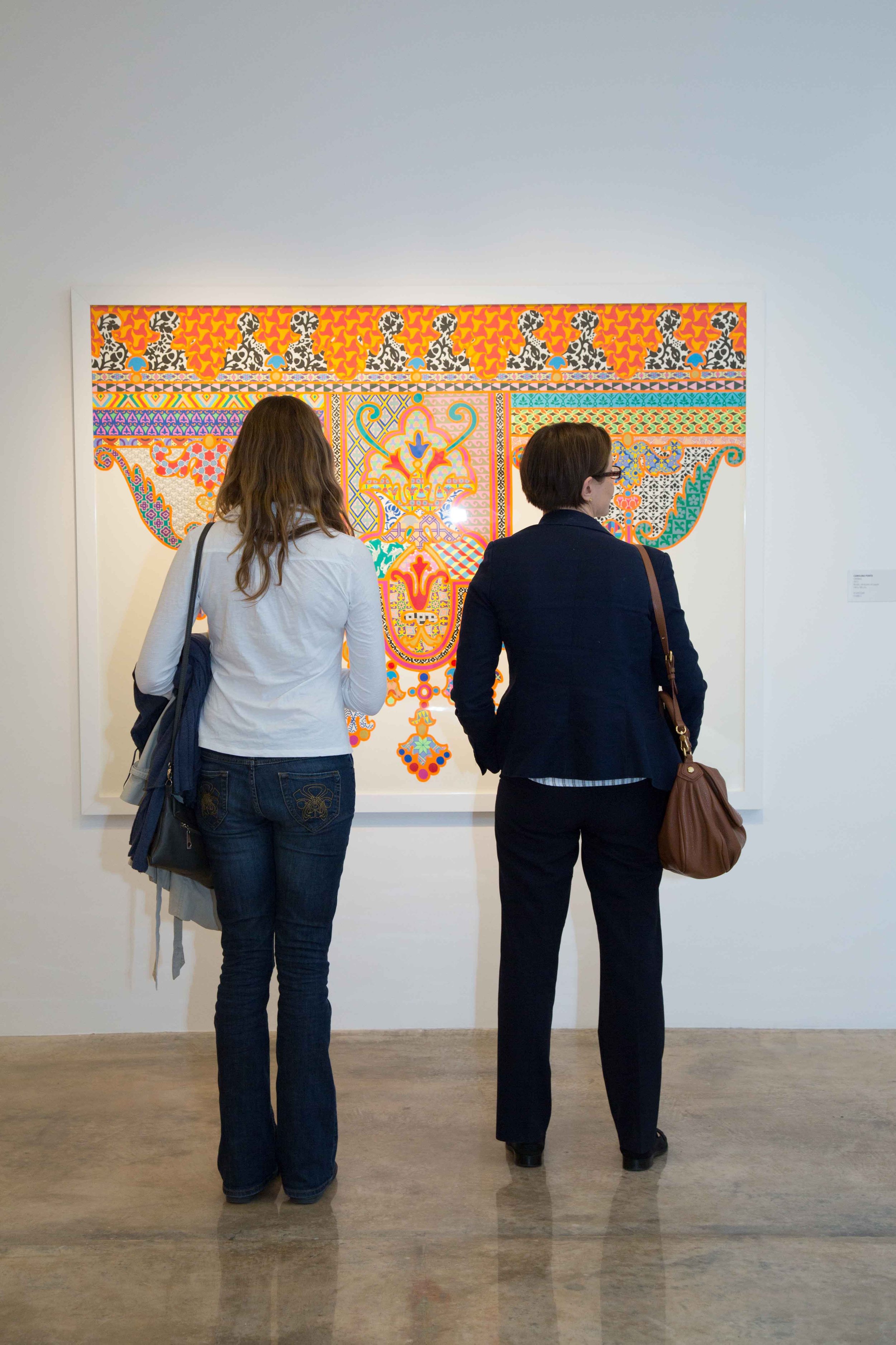 Two women look at colorful artwork in an art gallery.