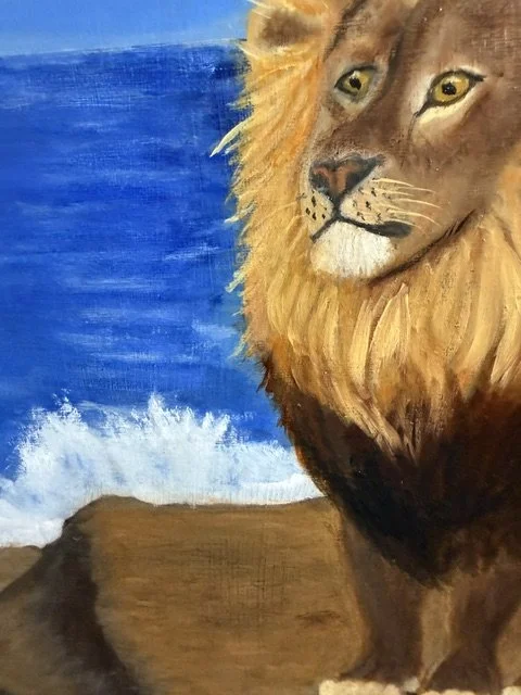 Close-up detail of the lion's face and golden mane, with the mountain ledge and ocean waves behind him in Moonlit Majesty by Bonnie Seide.