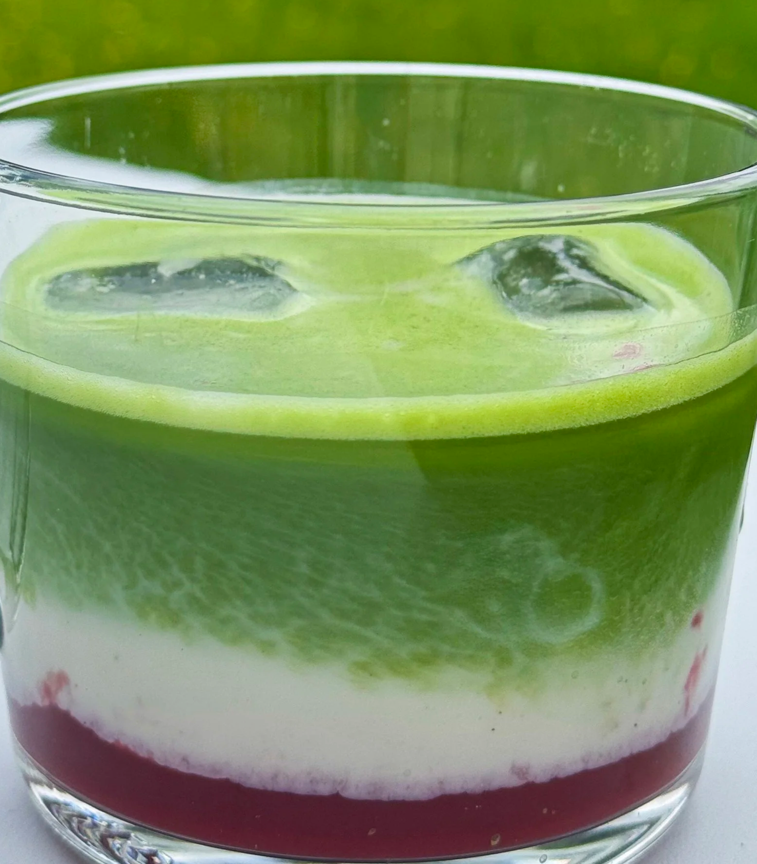 Close-up of a layered fruit and vegetable juice in a clear glass, with green, white, pink, and purple layers.