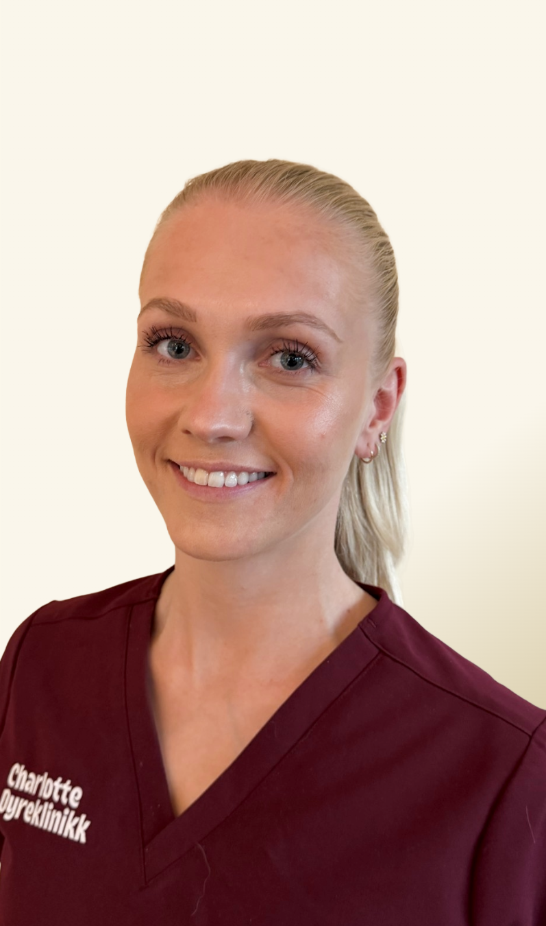 Portrettbilde av Mia i burgunderrød klinikkuniform med Charlotte Dyreklinikk-logo. Hun smiler mot kameraet foran en lys, nøytral bakgrunn.