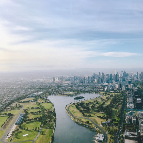 Aerial view of a city skyline with tall skyscrapers, a large park with a winding river, and cloudy sky.