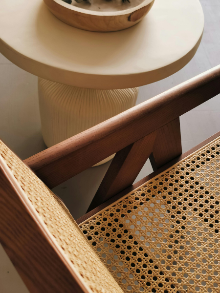 Close-up view of a wooden chair with woven cane seat, a round cream-colored side table, and part of a bowl on the table.