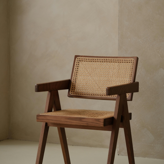 A wooden chair with woven cane backrest and seat, positioned near a corner with beige textured walls.