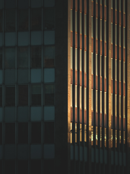 Close-up of two modern building facades with glass windows and vertical wooden slats, with sunlight illuminating part of the right building.