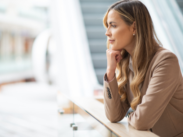 A woman sitting at a table, looking thoughtfully to the side in a brightly lit space.