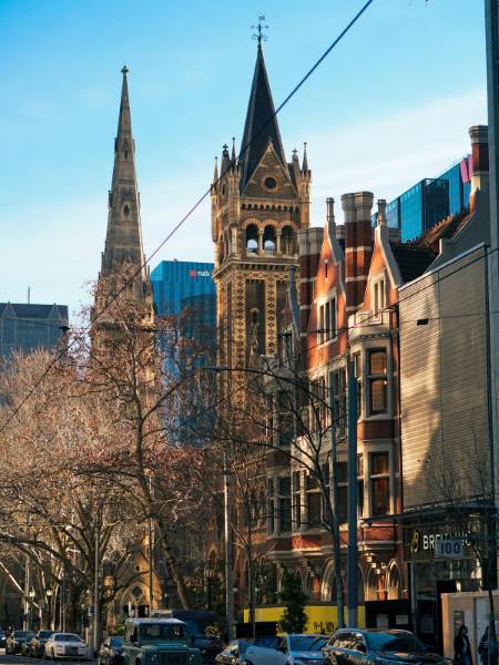 City street with historic church buildings, trees, cars, and modern buildings in the background.