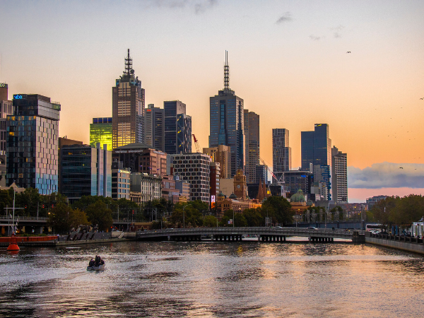 Sydney skyline at sunset with river in foreground and boats on water.