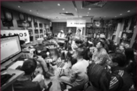 A group of people attending a seminar or presentation in a room with shelves and framed pictures on the walls.