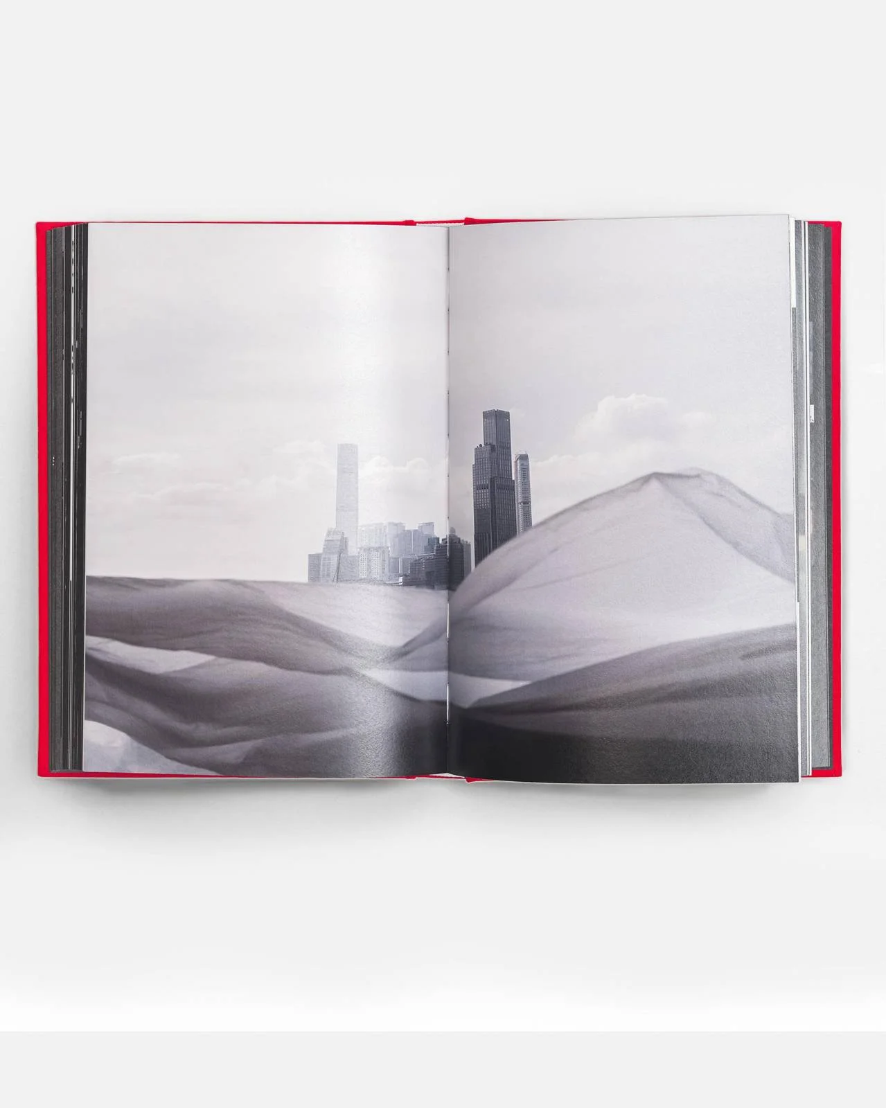 Open photo book showing a black and white landscape with sand dunes in the foreground and city skyscrapers in the background.