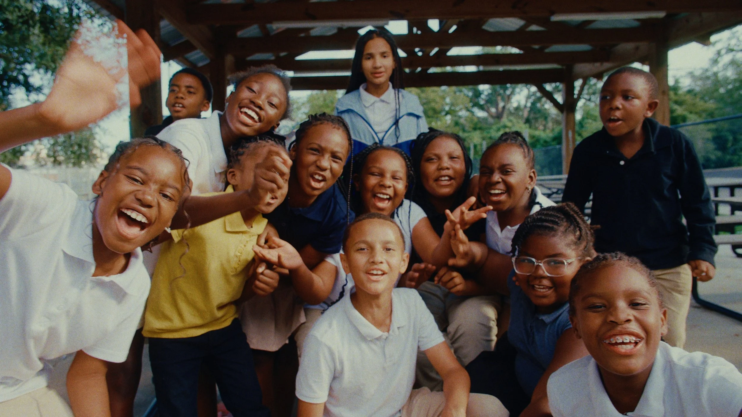 Group of children and a woman smiling and having fun in an outdoor playground, taken under a wooden pavilion.