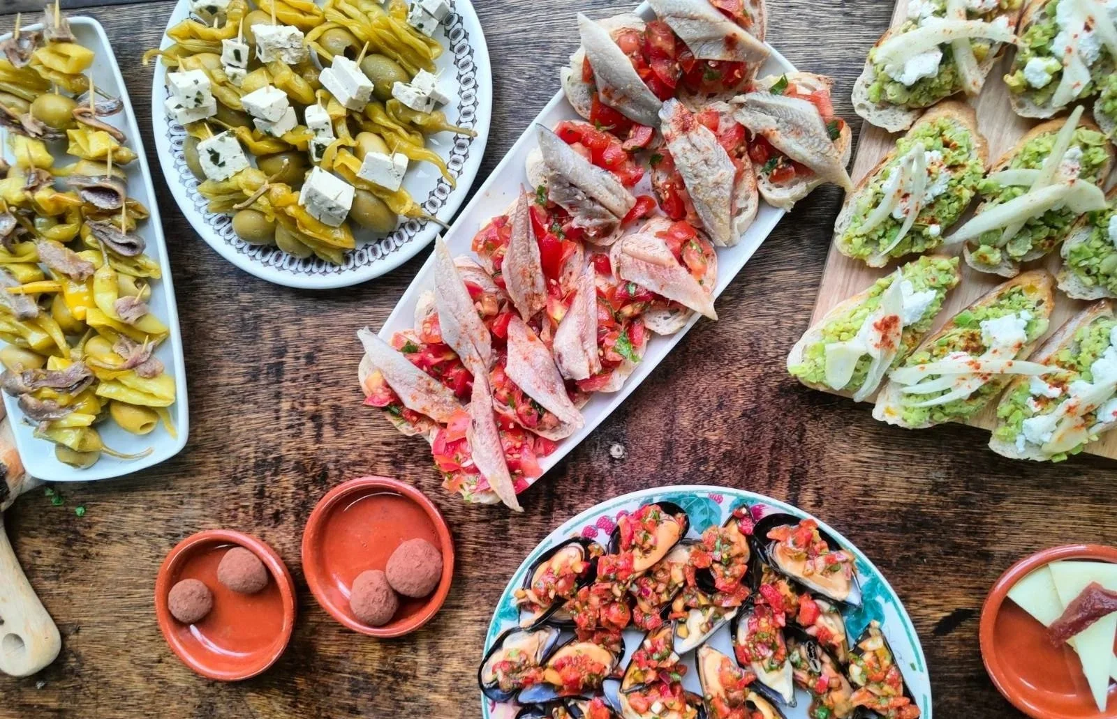 Assorted Mexican appetizers on a wooden table including stuffed jalapeños, pickled vegetables, shrimp tostadas, and mussels topped with salsa.