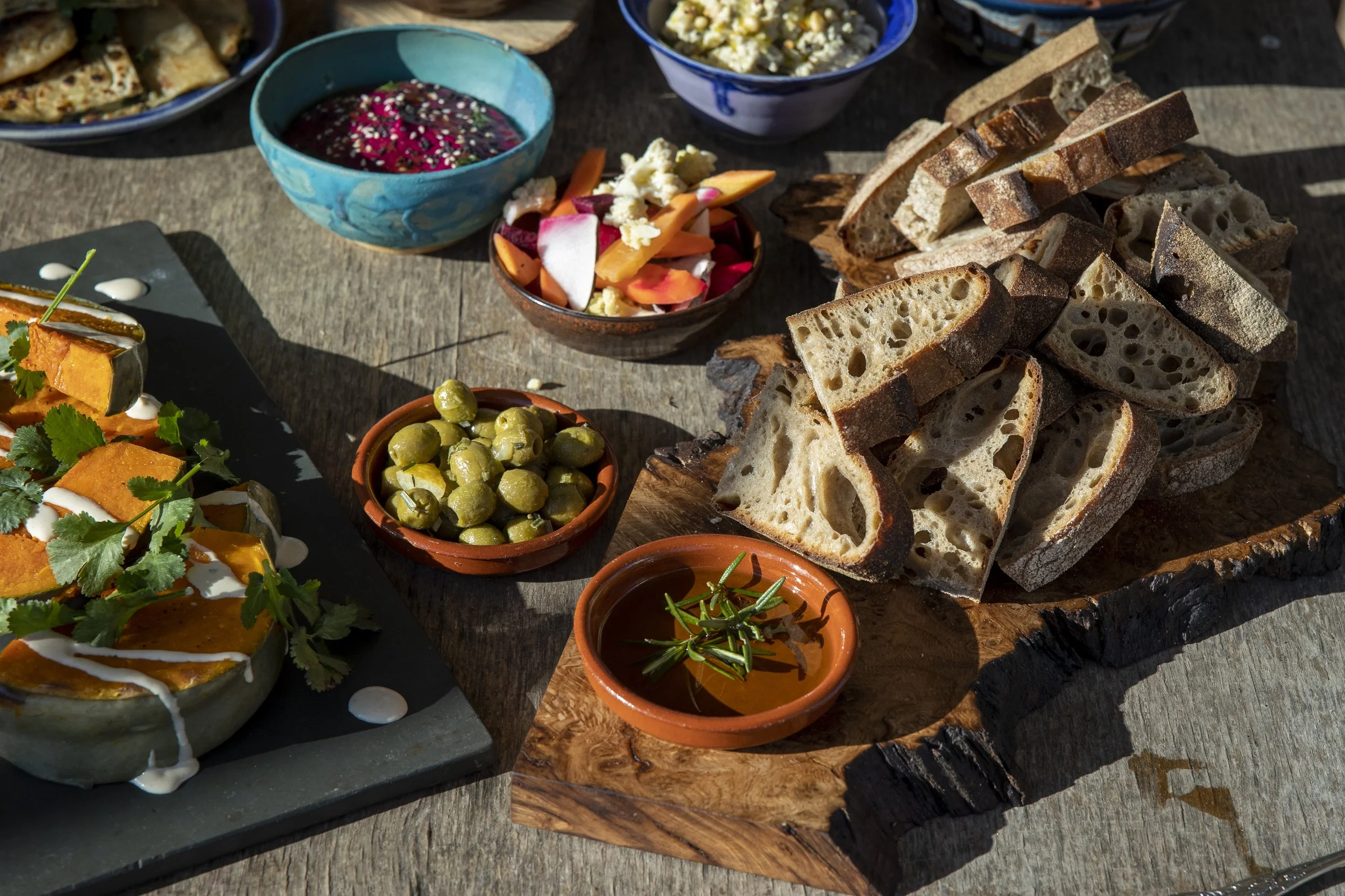 Various Indian dishes and snacks on a rustic wooden table, including bread, pickles, dips, and side dishes in small bowls.