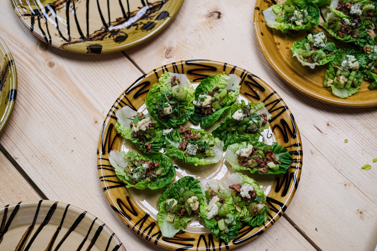 A plate of lettuce wraps filled with ground beef, chopped onions, and crumbled blue cheese on a wooden table.