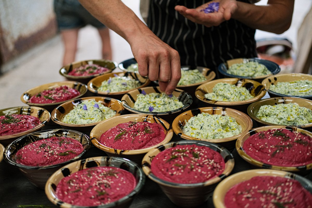 A person serving colorful dips in various bowls on a table.