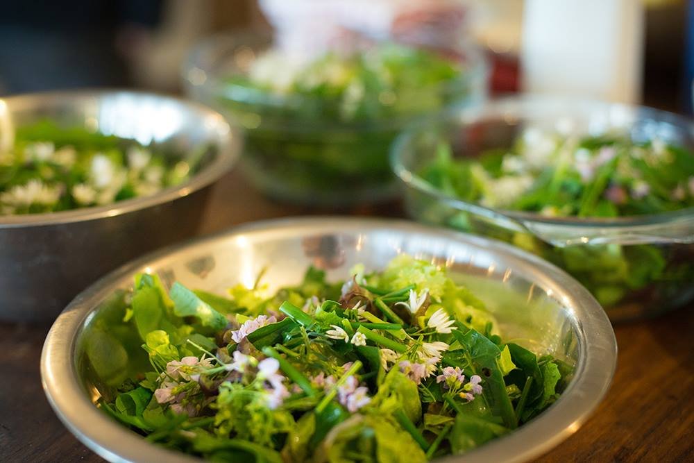 Various bowls filled with fresh mixed salad greens and edible flowers on a wooden table.