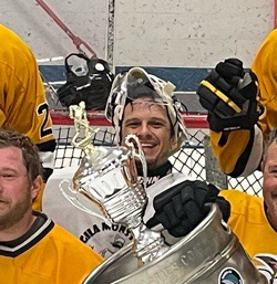 Hockey players celebrating with a large trophy after a game, smiling and holding it up.
