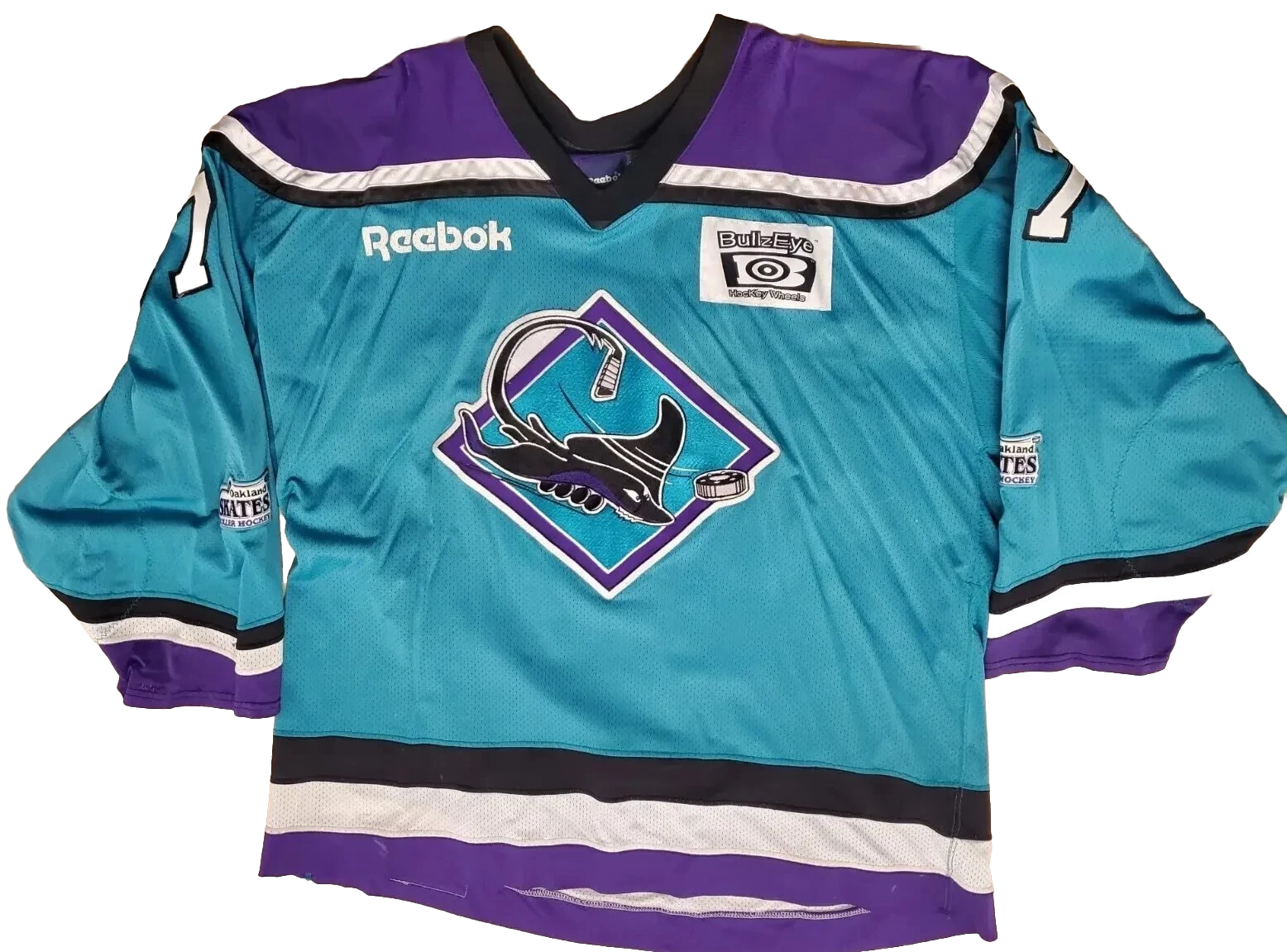 A hockey jersey with teal, purple, white, and black colors, featuring team logos and sponsorship patches.