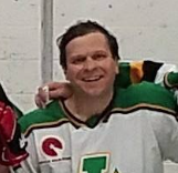 A man in a green and white hockey jersey smiling at the camera.