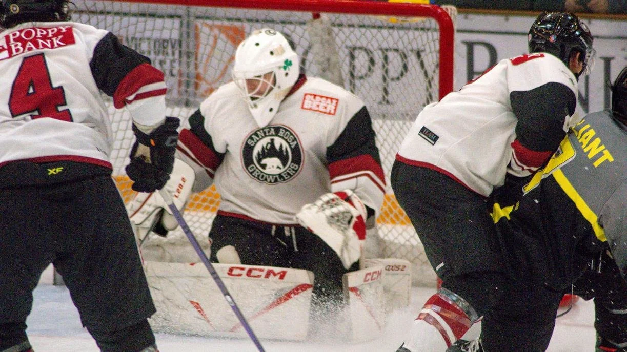 Hockey play in action on the ice, with a goalie in front of the net, and players trying to score or defend.