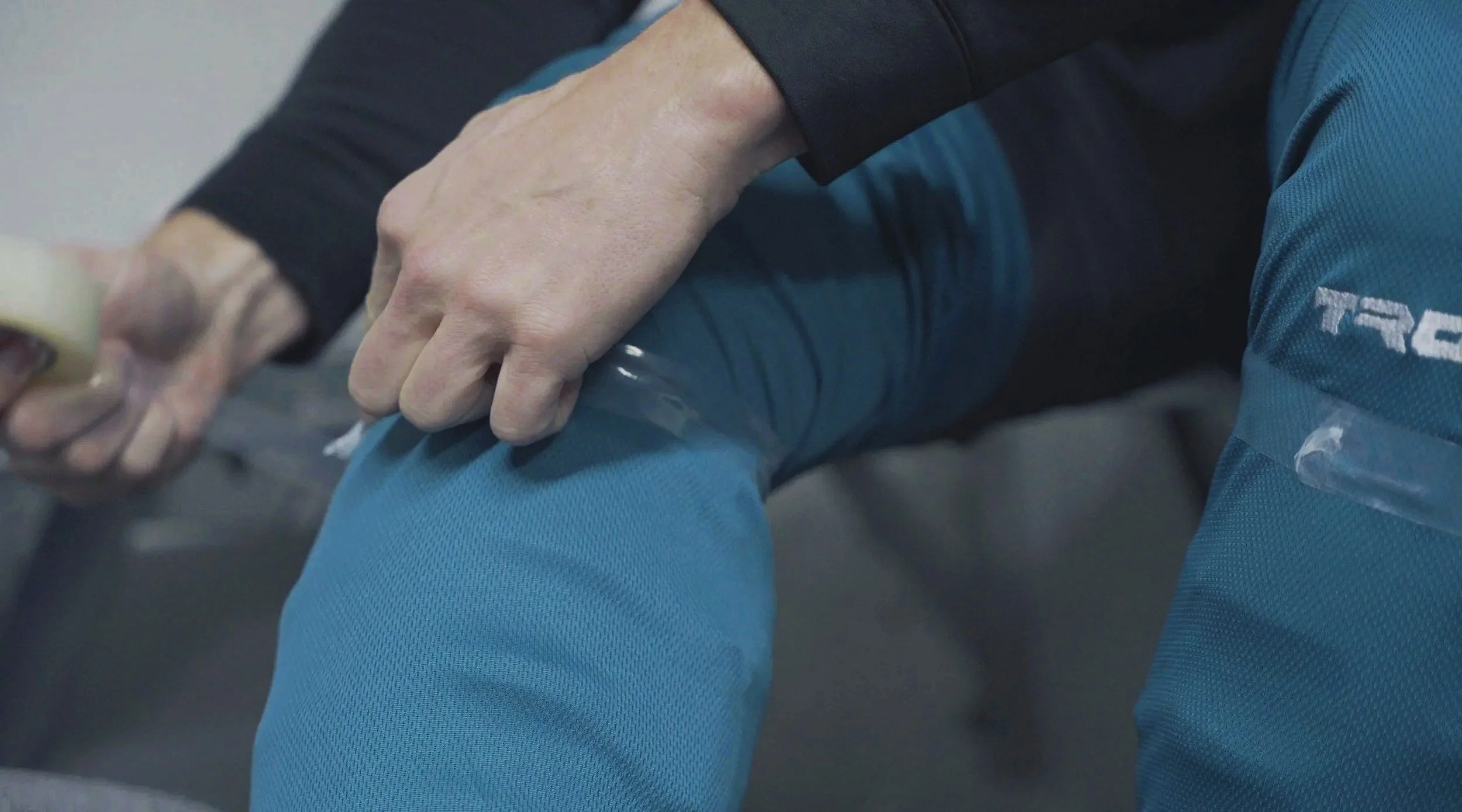 A person in a black long sleeve shirt has their leg straight out and is applying medical tape to it