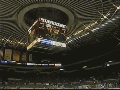 Interior view of a sports arena with a large electronic scoreboard displaying information and advertisements.