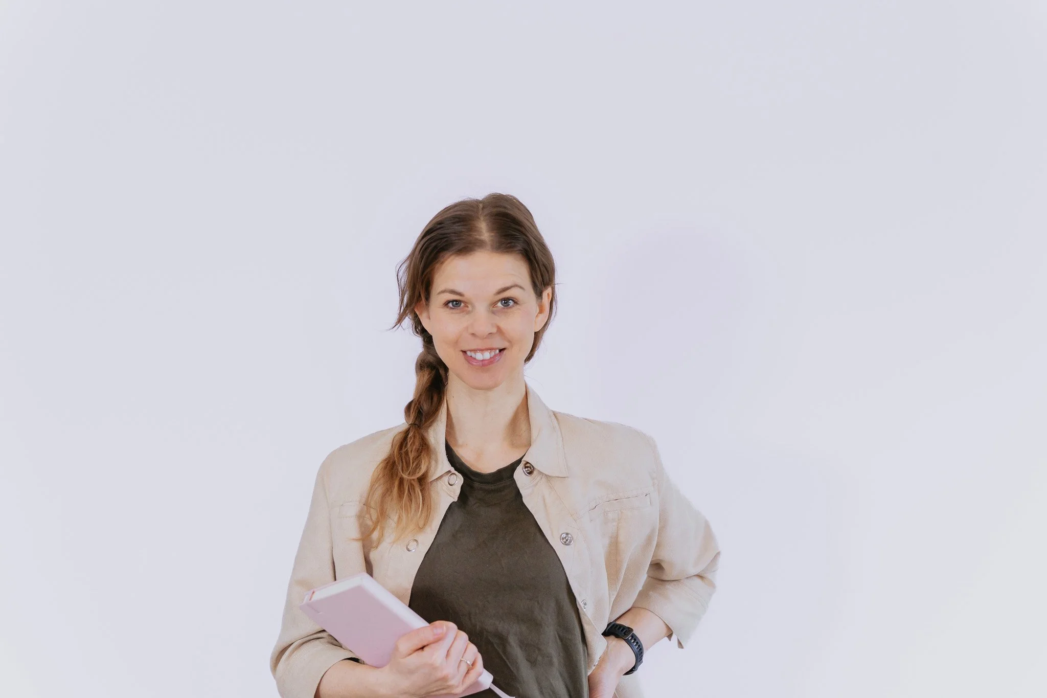 Ung kvinna med långt lockigt hår, blond och brun, håller en rosa anteckningsbok och ler mot kameran.