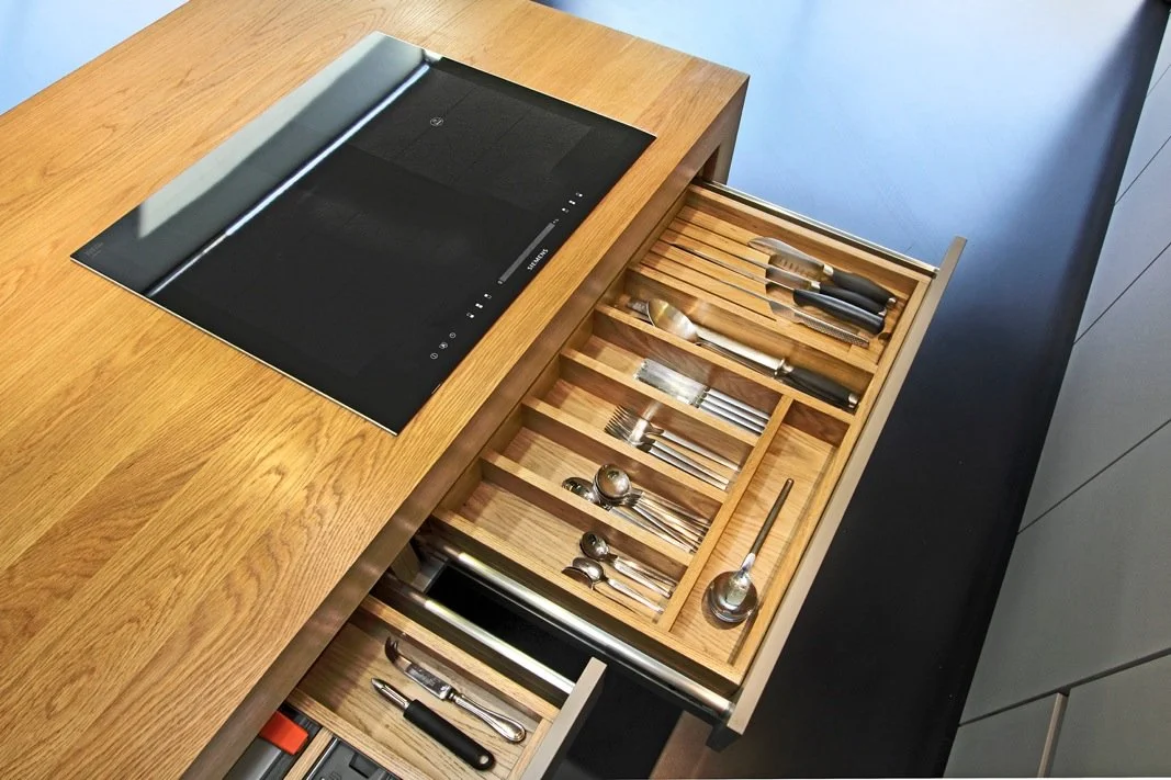 Open kitchen drawer with utensils and a black induction cooktop on a wooden countertop.