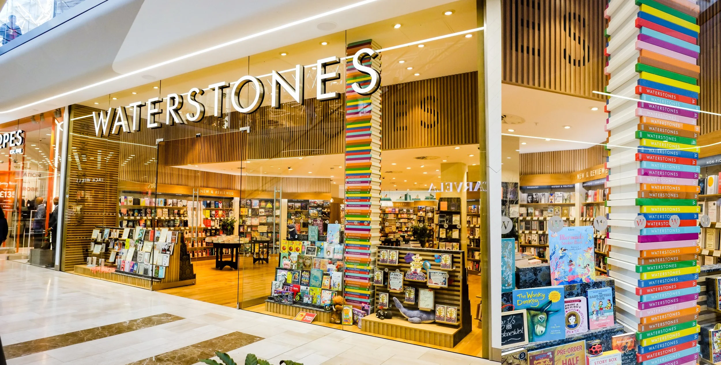 View of Waterstones bookstore inside a shopping mall, with a large colorful book stack outside.