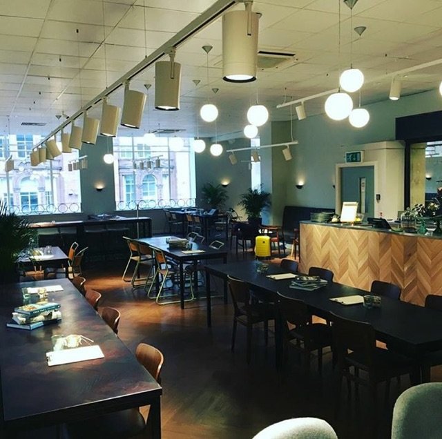 Interior of a modern restaurant with dark wooden tables, chairs, and stylish pendant and spherical ceiling lights, large windows, and a chevron-patterned wooden counter.