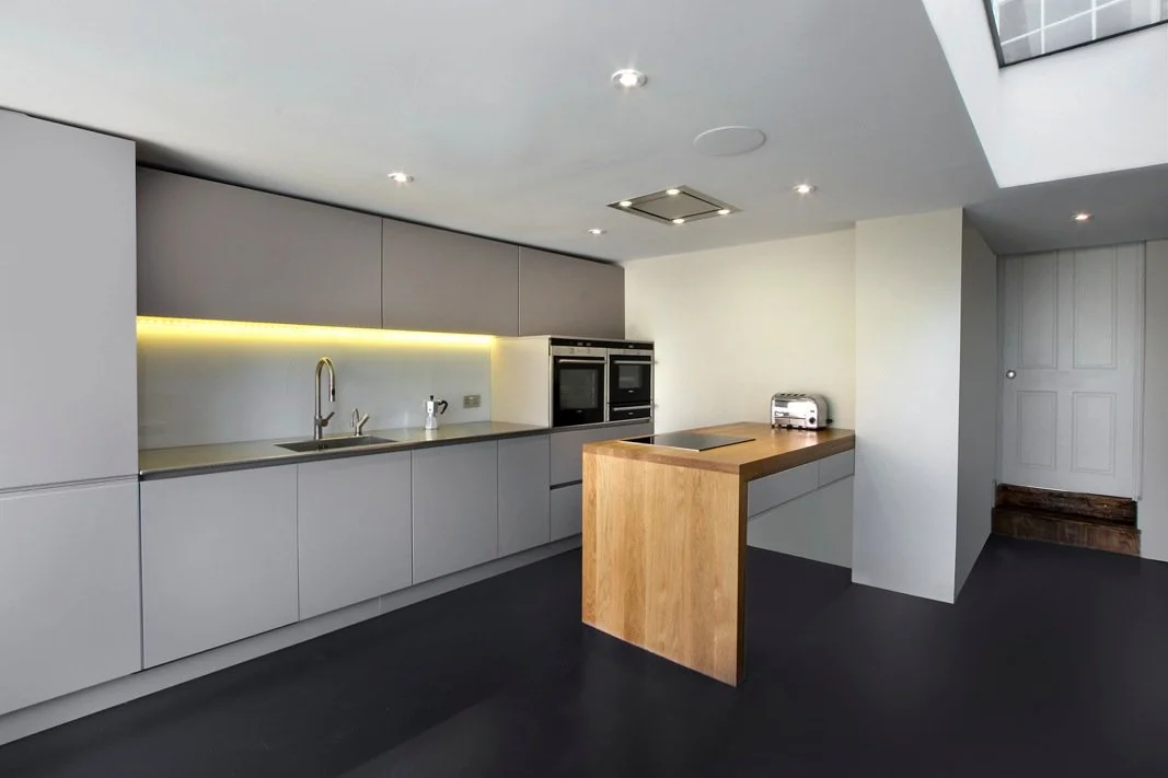 Modern kitchen with gray cabinets, built-in appliances, a sink, and a wooden breakfast bar.
