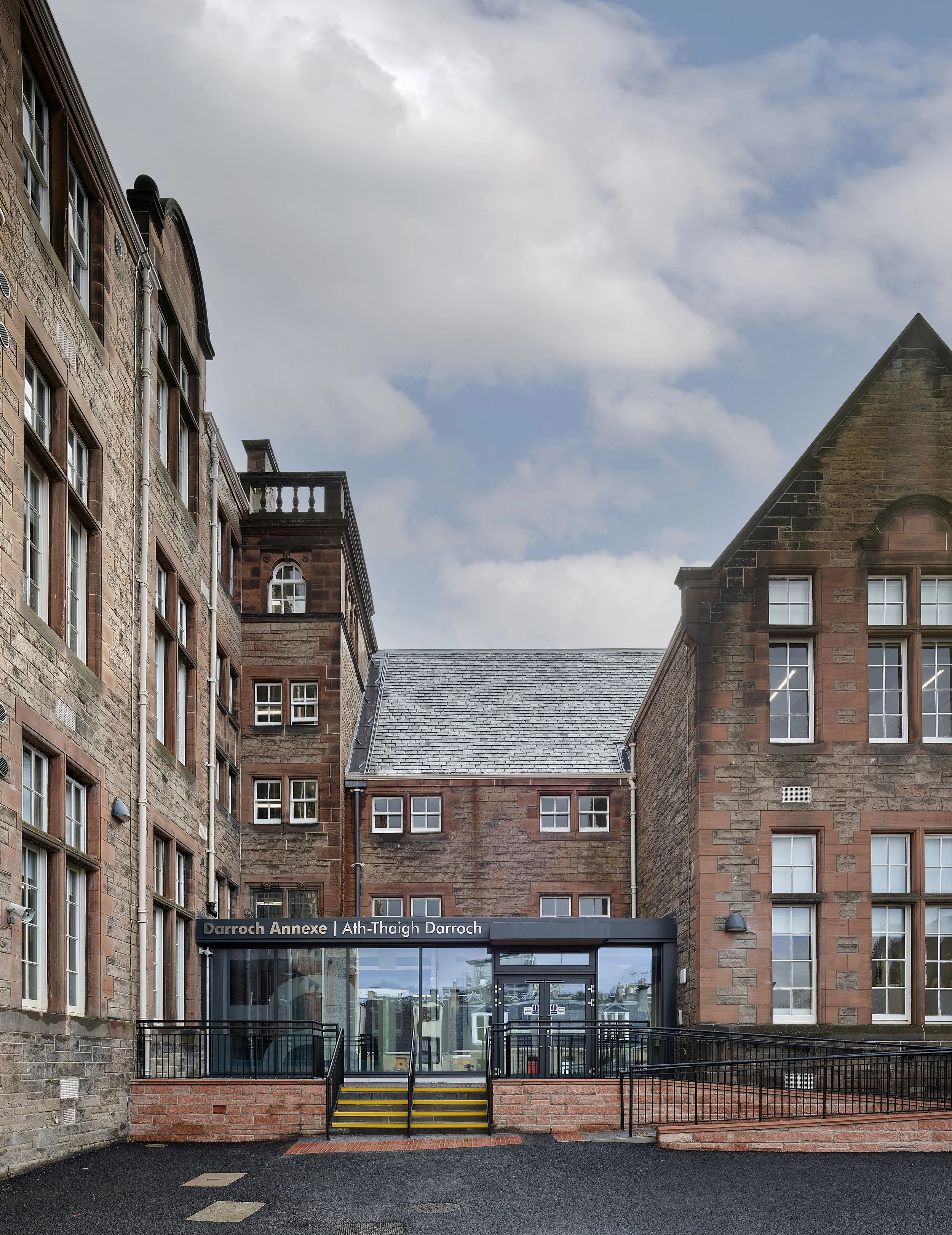 Exterior view of Darroch Annexe building with brick and stone facade, glass entrance, and stairs, under a partly cloudy sky.