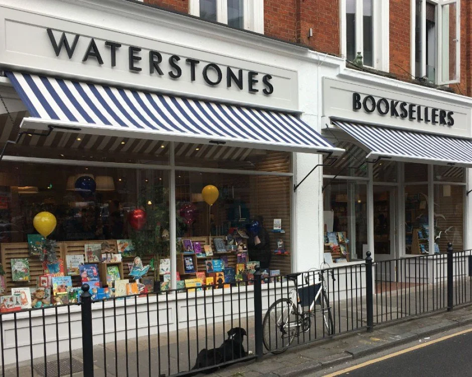 Outside of Waterstones bookstore with books on display in the window and a bicycle parked against a black fence.