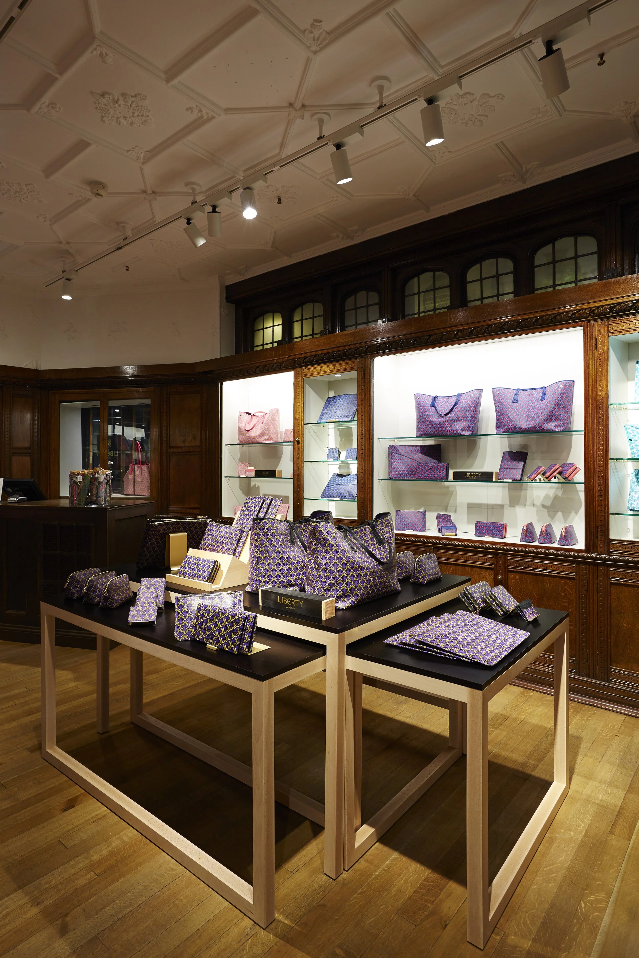 Display of purple and pink patterned bags, wallets, and accessories in a store.