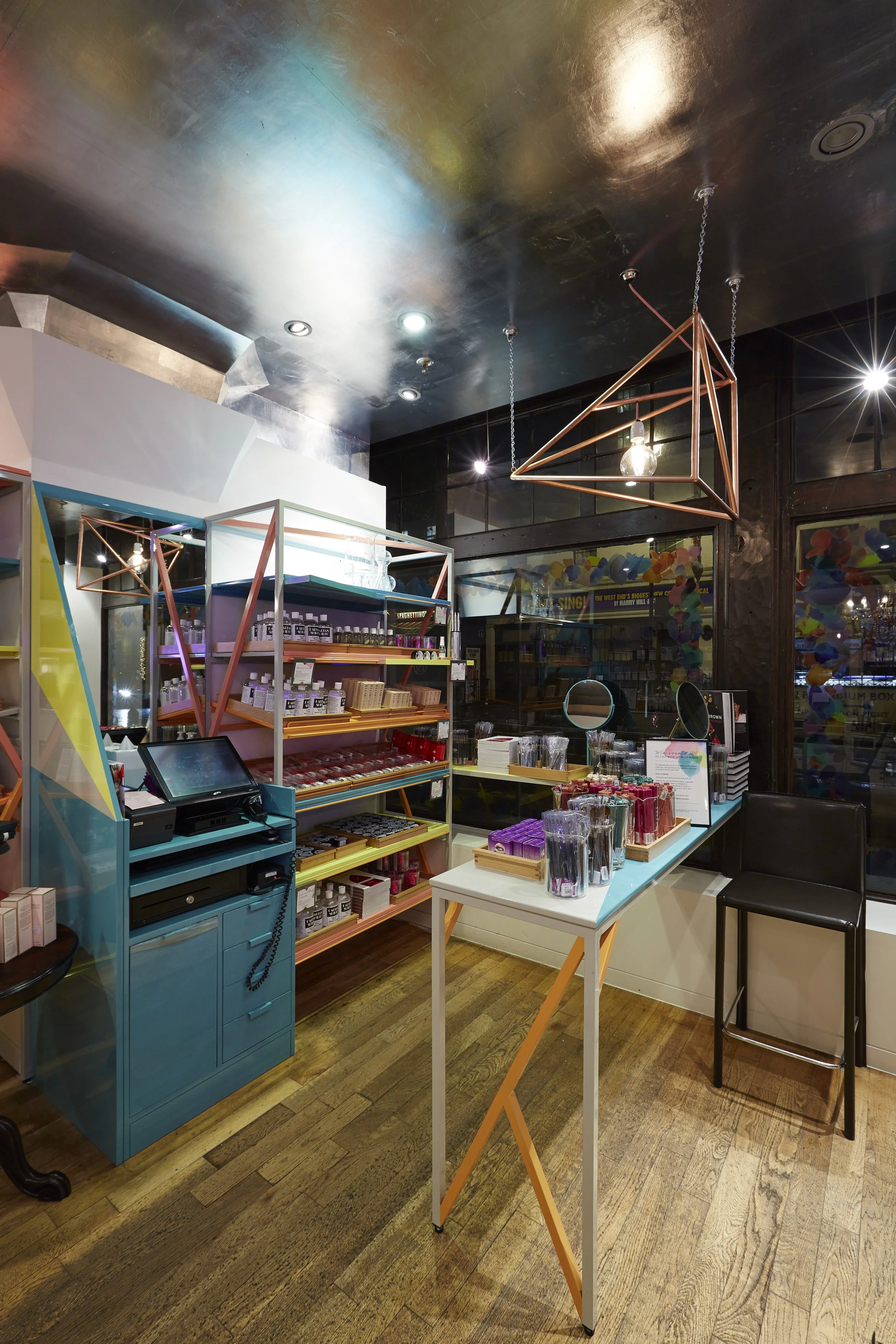 Interior of a retail store with colorful shelving, a cash register, and decorative geometric lighting fixtures hanging from a dark ceiling
