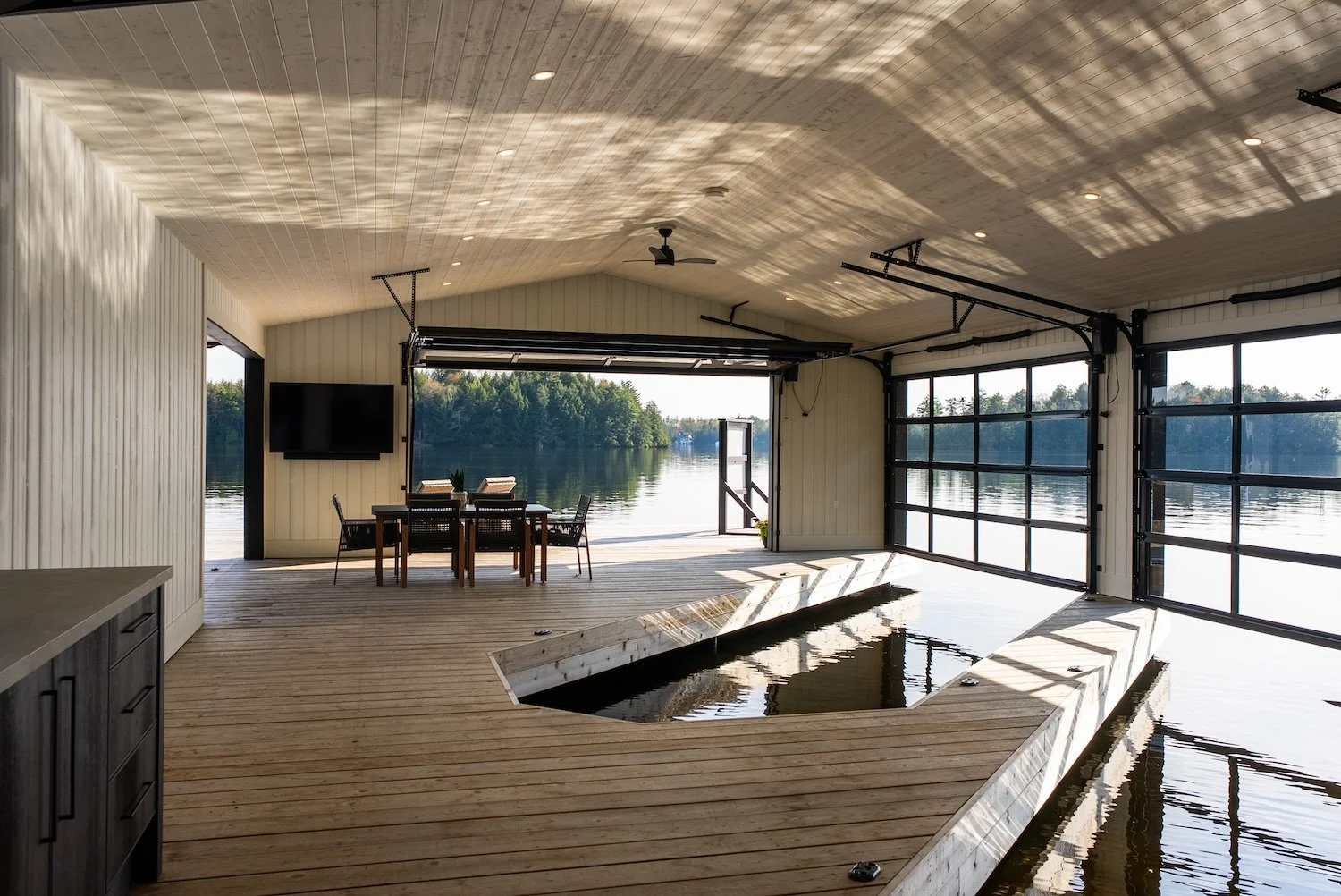 Modern boathouse interior with open garage doors overlooking a calm lake and dock.
