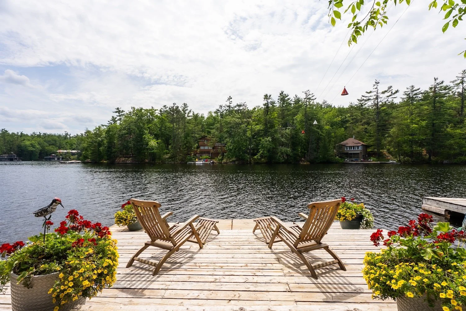 Lakeside dock with wooden chairs overlooking calm water and forested shoreline.