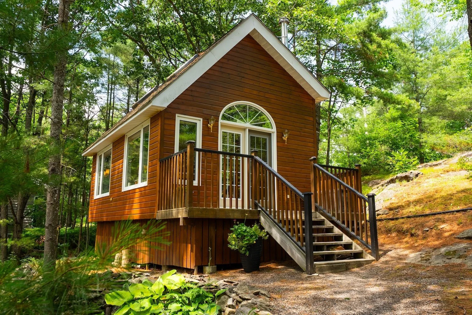 Wood-clad cottage exterior with front deck and stairs surrounded by trees.