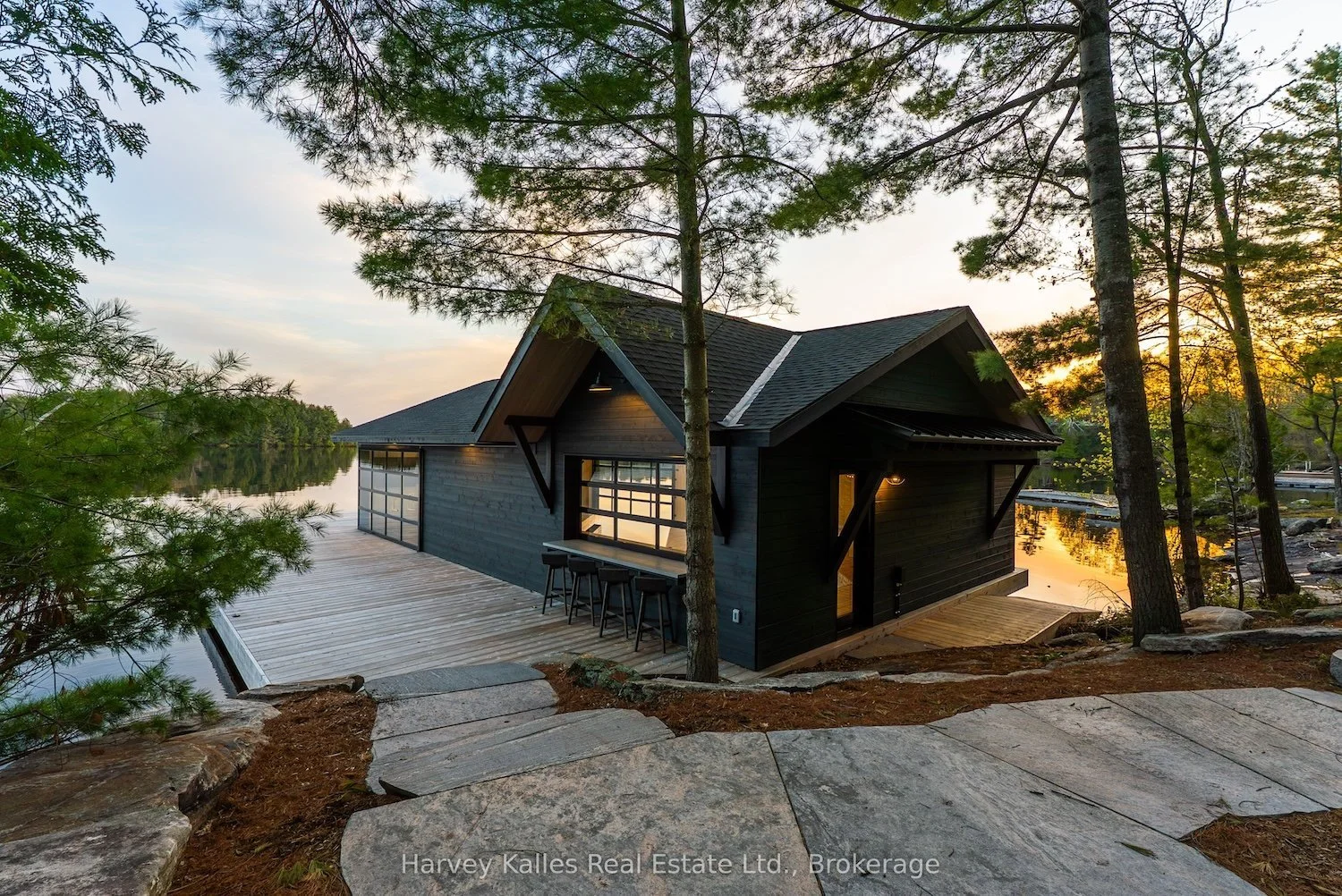 Luxury Lake Muskoka boathouse with outdoor bar and dock at sunset, listed by Gini Kelly, Harvey Kalles Real Estate