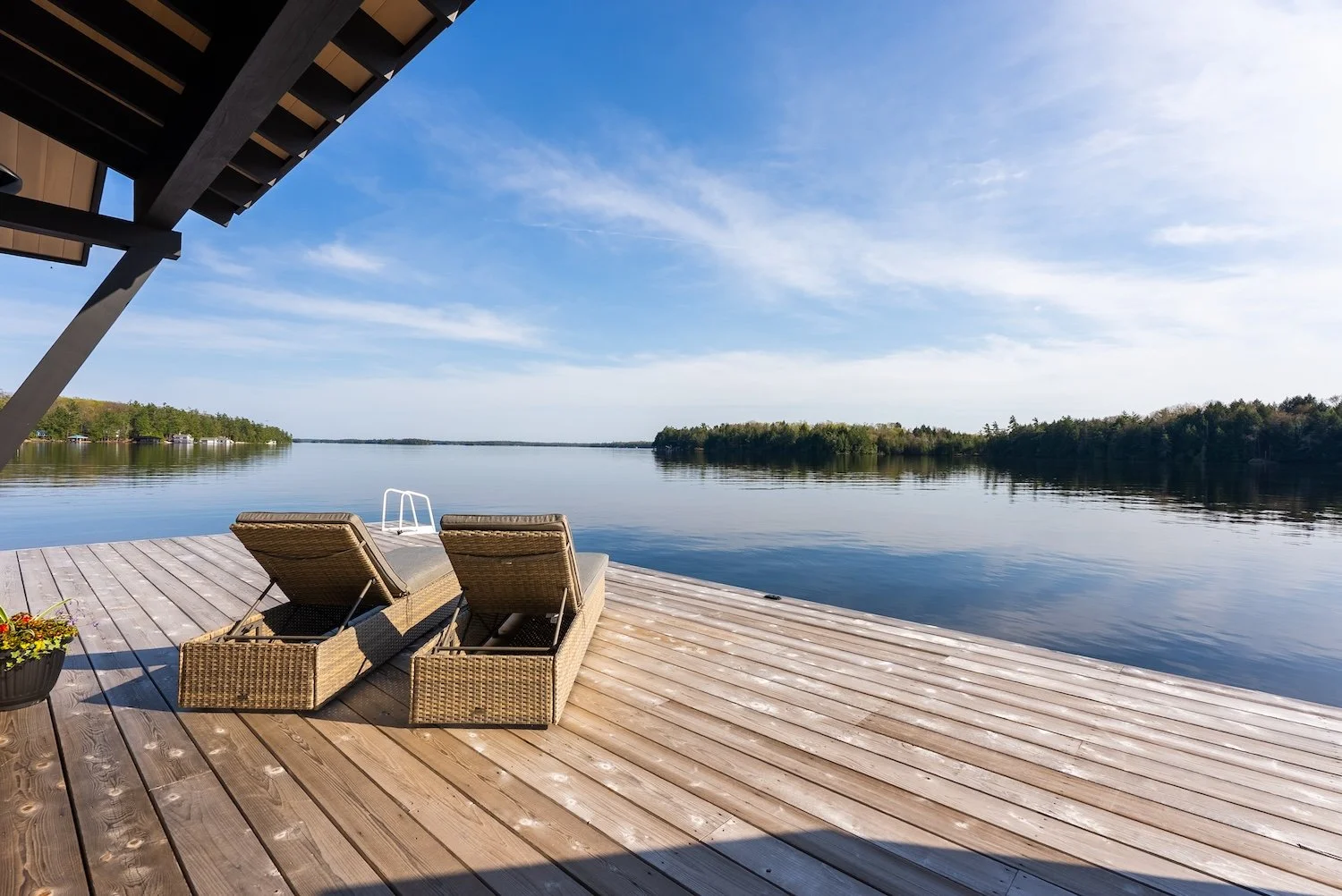 Waterfront dock with lounge chairs overlooking calm lake in Muskoka, Ontario.