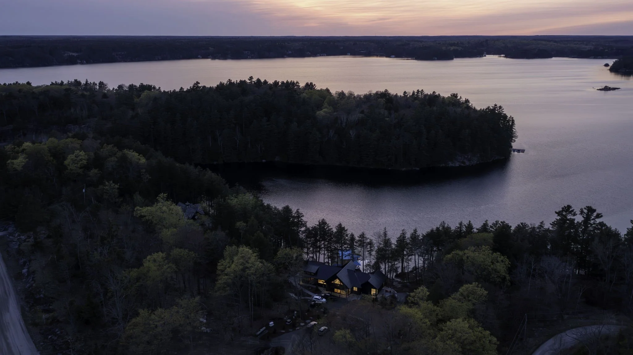 Aerial view of Muskoka waterfront property at sunset with forested shoreline and lake.