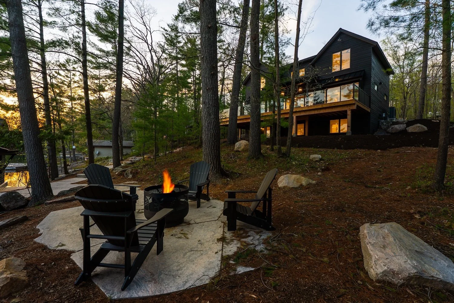 Modern Muskoka cottage in forest setting with outdoor fire pit and Adirondack chairs.